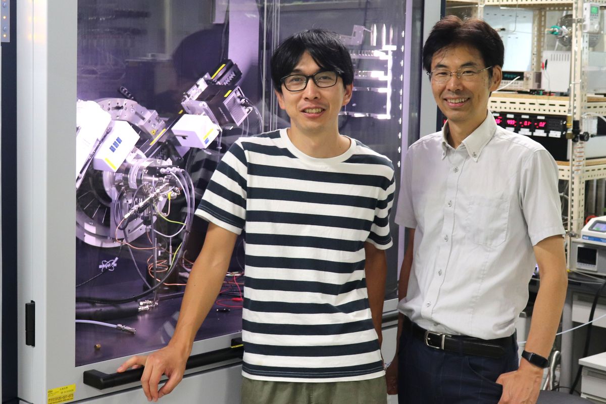 Junji Hyodo and Yoshihiro Yamazaki stand in front of a super-cool looking piece of equipment