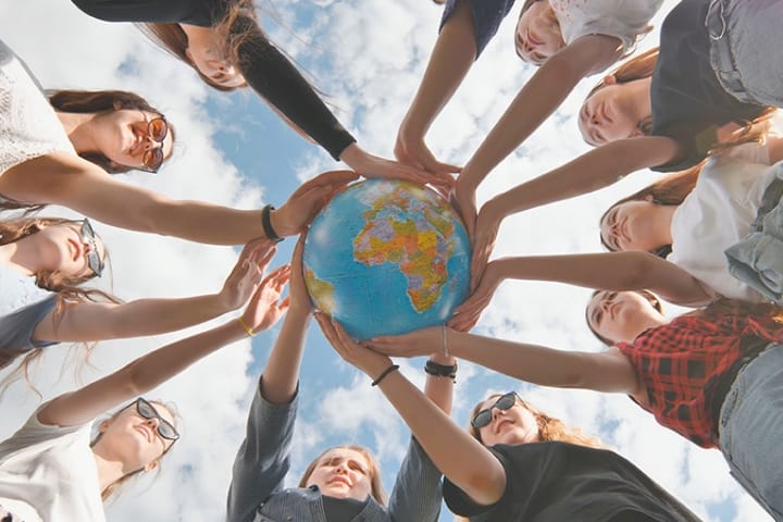 People in a circle with their hands on a globe in the middle